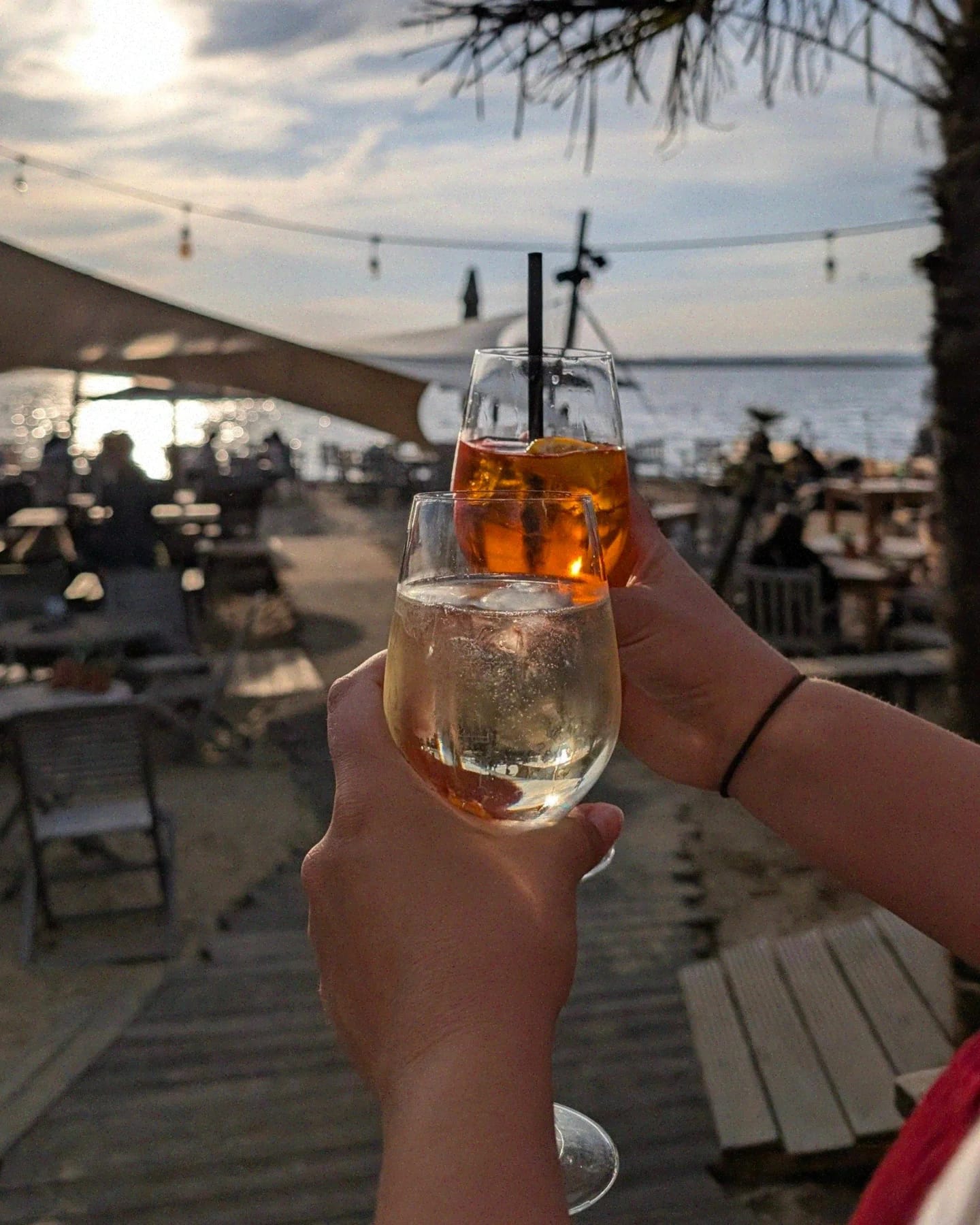 Zwei Gläser beim Anstoßen mit Blick auf die Beach Bar und den Dümmersee